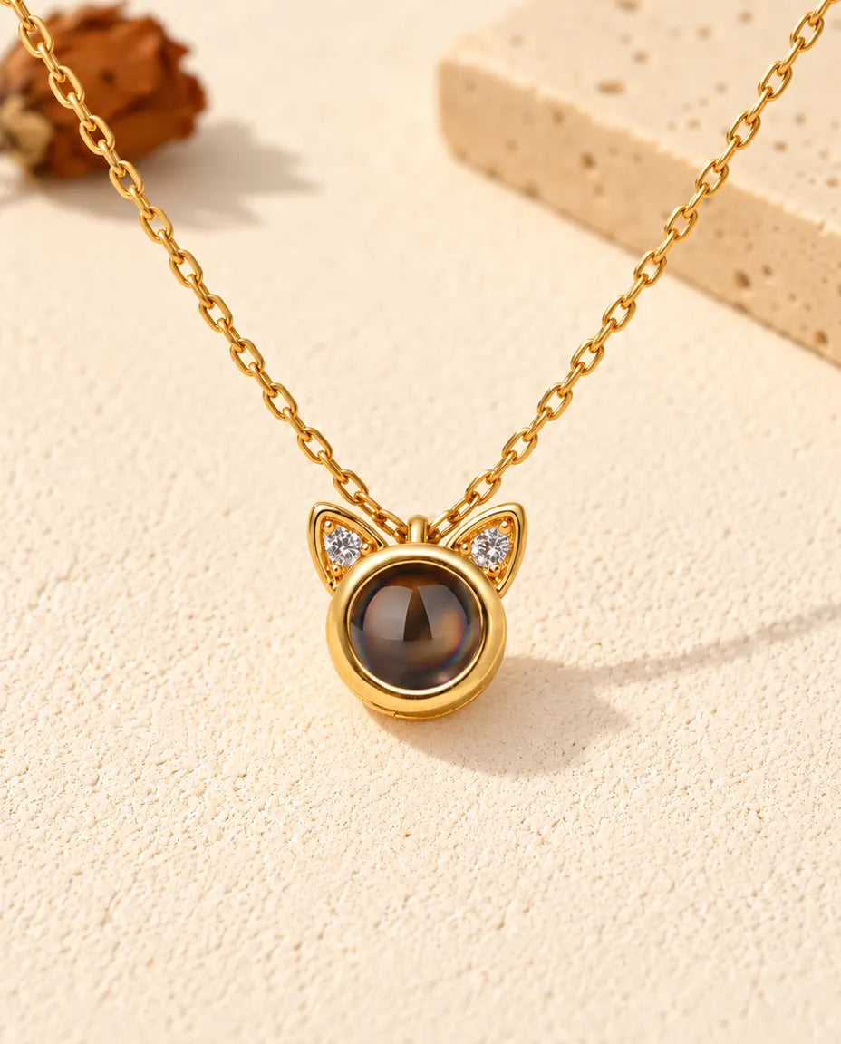 Vue de face du petit pendentif rond doré surmonté de deux oreilles de chat