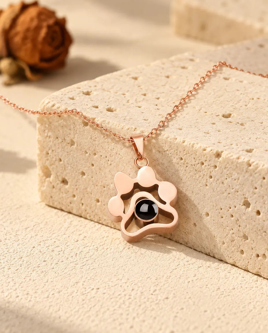 Collier patte couleur or rose posé sur un bloc de travertin
