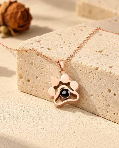 Collier patte couleur or rose posé sur un bloc de travertin