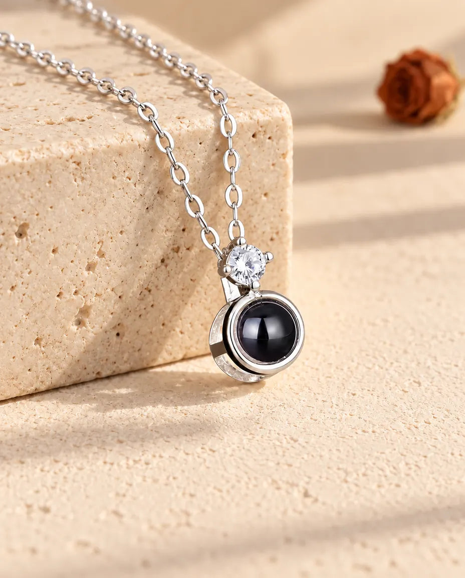 Collier solitaire argenté avec photo dans la pierre posé sur un bloc de travertin