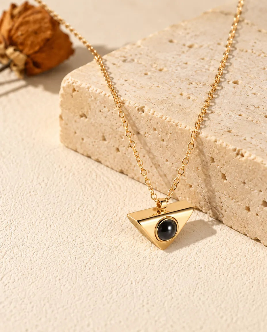Collier triangle doré avec photo dans la pierre posé sur un bloc de travertin