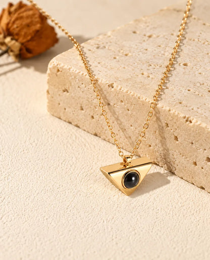 Collier triangle doré avec photo dans la pierre posé sur un bloc de travertin