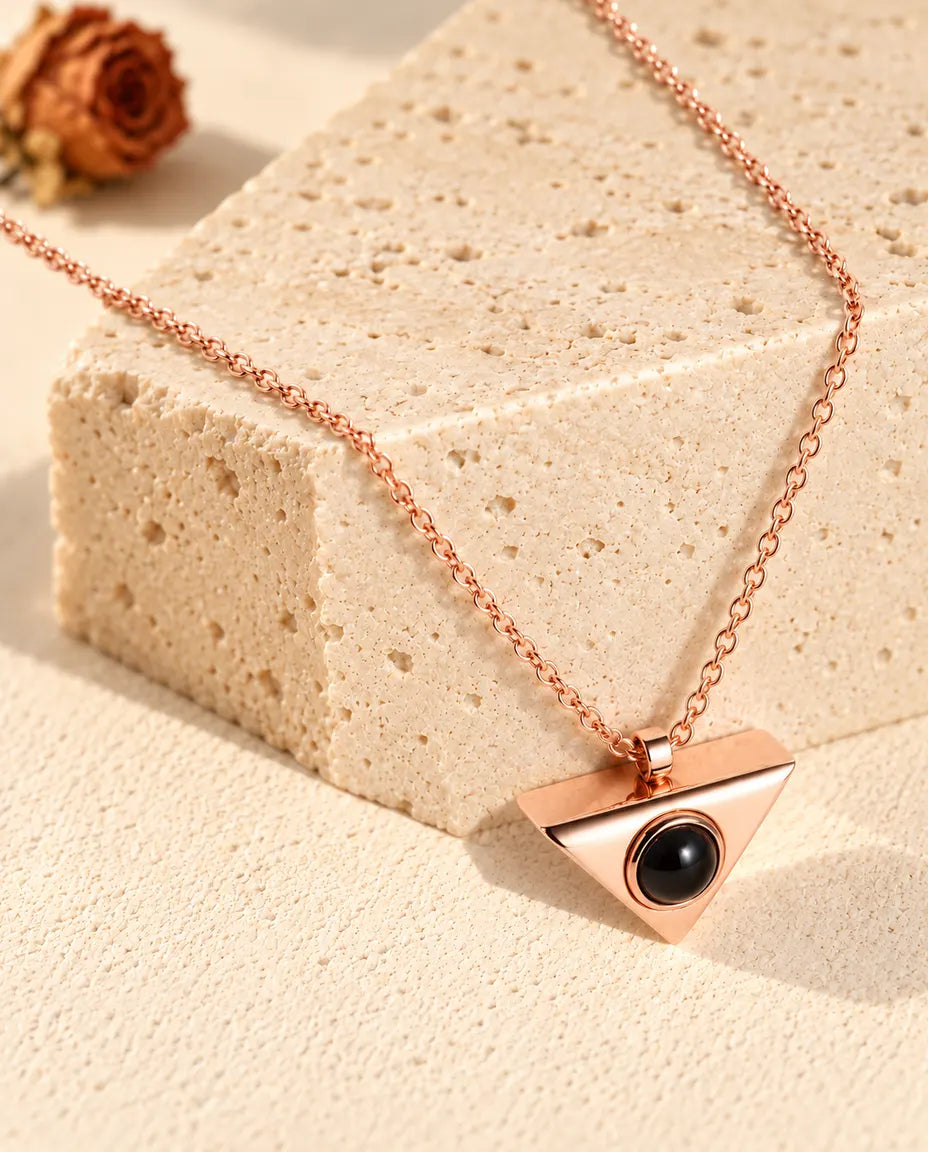 Collier triangle couleur or rose suspendu au-dessus d'un bloc de travertin