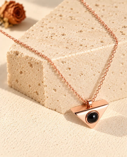 Collier triangle couleur or rose suspendu au-dessus d'un bloc de travertin