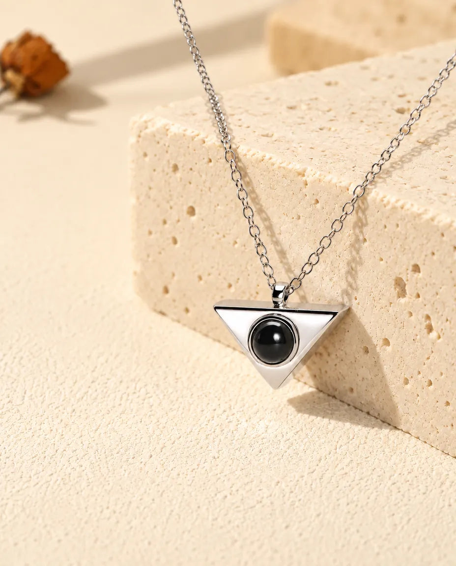 Pendentif triangle argenté avec sa pierre de projection vu de biais sur du travertin