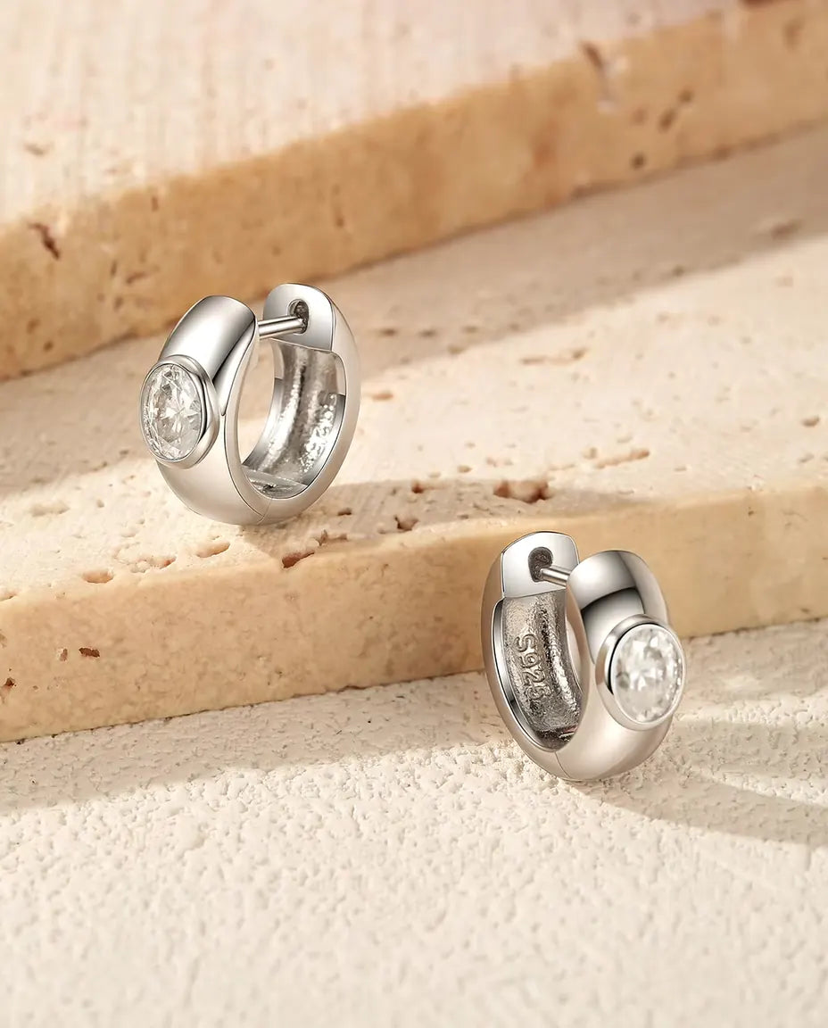 Boucles d’Oreilles Créoles Huggie Moissanite Ovale en Argent 925 - la paire posée sur des marches en travertin