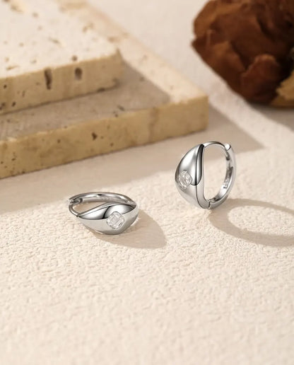 Boucles d’Oreilles Créoles Huggie Moissanite Taille Asscher en Argent 925 - la paire sur une surface claire texturée, l’une à plat et l’autre debout