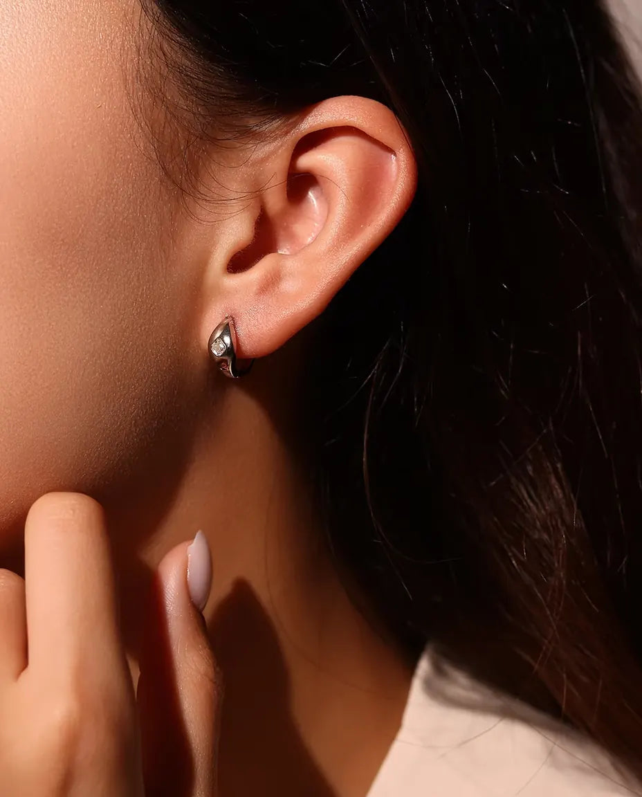 Boucles d’Oreilles Créoles Huggie Moissanite Taille Asscher en Argent 925 - portées à l’oreille par un mannequin, main près du visage