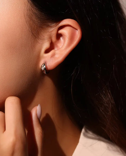 Boucles d’Oreilles Créoles Huggie Moissanite Taille Asscher en Argent 925 - portées à l’oreille par un mannequin, main près du visage