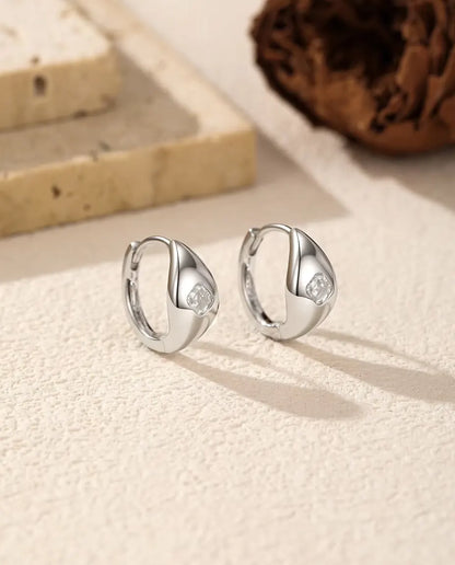 Boucles d’Oreilles Créoles Huggie Moissanite Taille Asscher en Argent 925 - la paire posée côte à côte sur une surface claire texturée