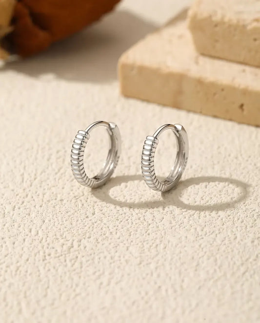 Boucles d’Oreilles Créoles Huggie Striées en Argent 925 - la paire posée côte à côte sur une surface claire texturée