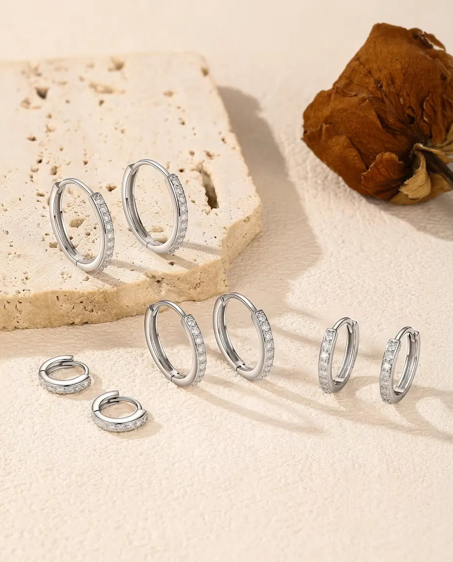 Boucles d’Oreilles Créoles Moissanite en Argent 925 - les cinq tailles disposées sur une surface claire près d’une dalle de travertin