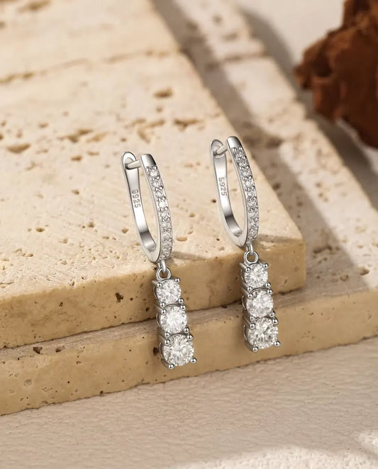 Boucles d’Oreilles Créoles Pendantes Trois Moissanites en Argent 925 - la paire suspendue au rebord d’une dalle de travertin