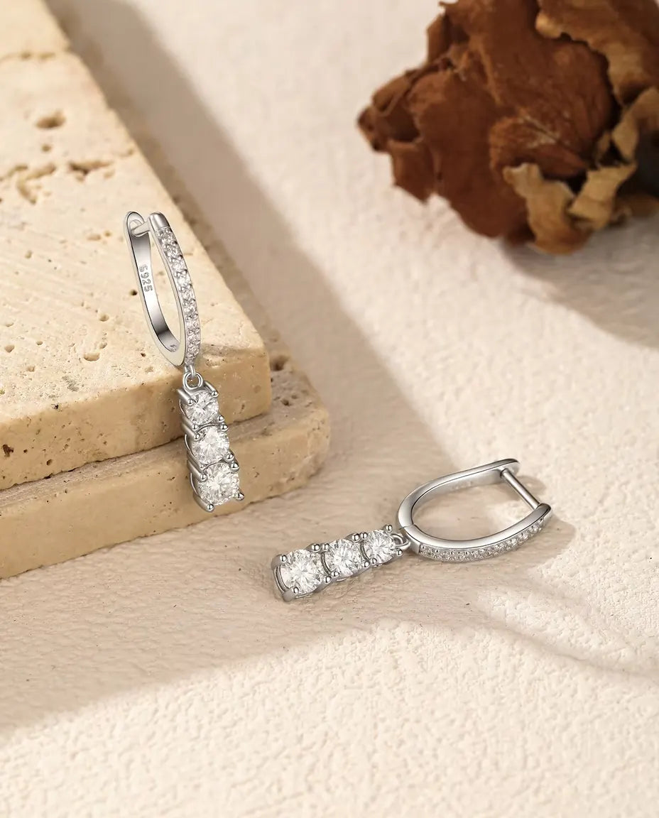 Boucles d’Oreilles Créoles Pendantes Trois Moissanites en Argent 925 - une boucle suspendue à une dalle de travertin, l’autre posée à côté