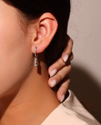 Boucles d’Oreilles Créoles Pendantes Trois Moissanites en Argent 925 - portées à l’oreille par un mannequin, doigts sur le cou
