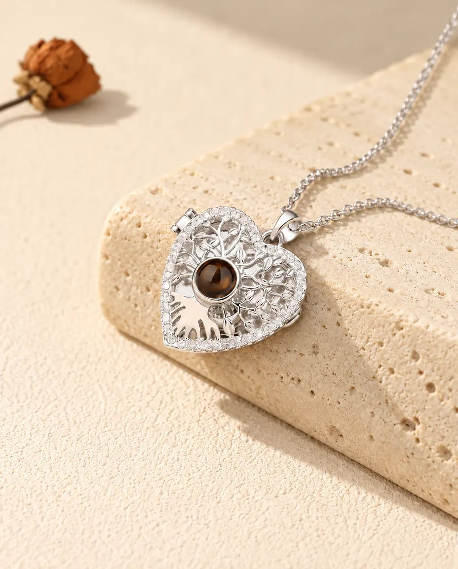 Collier médaillon cœur arbre de vie personnalisé argenté avec pierre de projection brune, posé sur un bloc de travertin