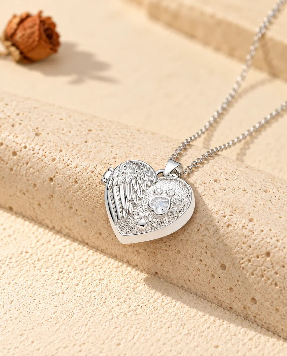 Collier personnalisé médaillon photo cœur aile d'ange et patte, couleur argentée, posé contre un bloc de travertin
