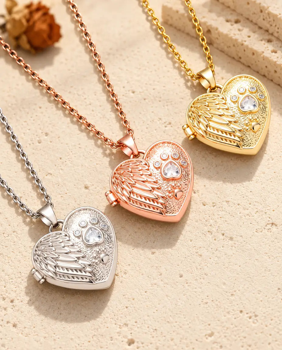 Le médaillon photo cœur aile d'ange et patte en argenté, couleur or rose et doré, posé en diagonale sur du plâtre crème