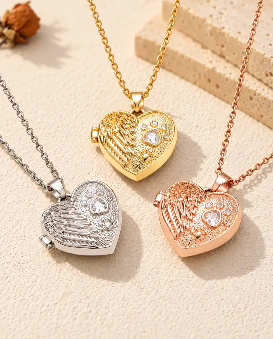 Les trois couleurs du collier médaillon photo cœur aile d'ange et patte disposées sur du plâtre