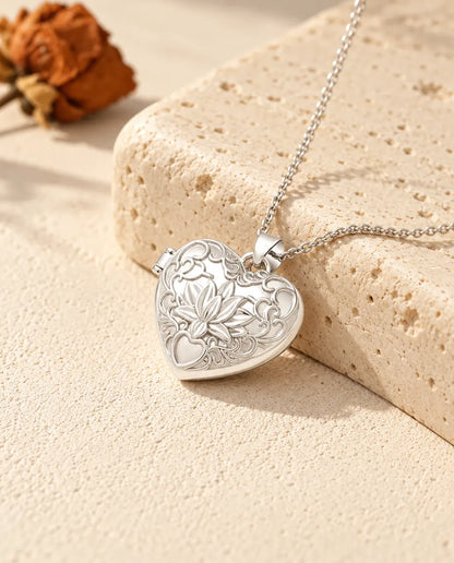 Collier personnalisé médaillon photo cœur fleur de lotus, couleur argentée, posé contre un bloc de travertin