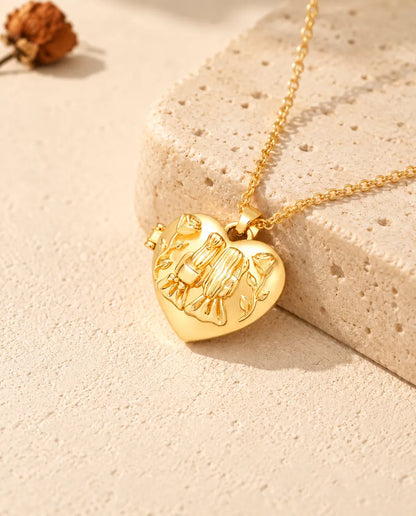 Collier médaillon photo cœur sœurs doré posé sur un bloc de travertin
