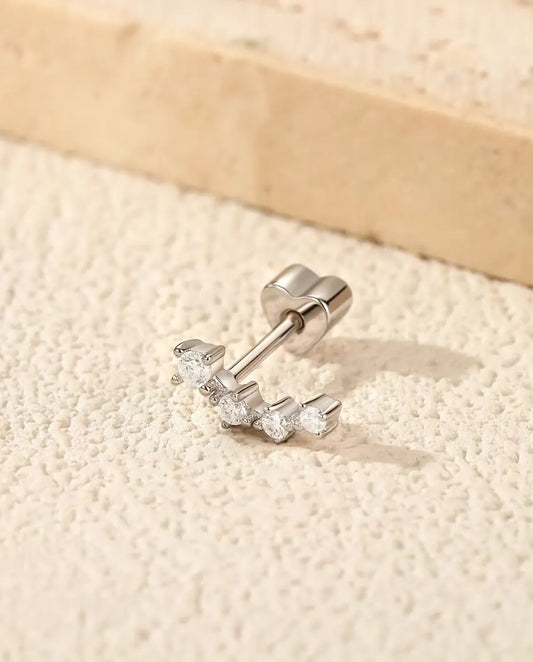 Puces d’Oreilles Grimpantes Moissanite en Argent 925 - posée sur une surface claire texturée près d’une dalle de travertin