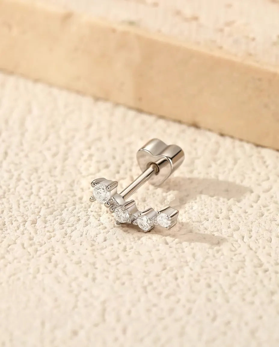 Puces d’Oreilles Grimpantes Moissanite en Argent 925 - posée sur une surface claire texturée près d’une dalle de travertin