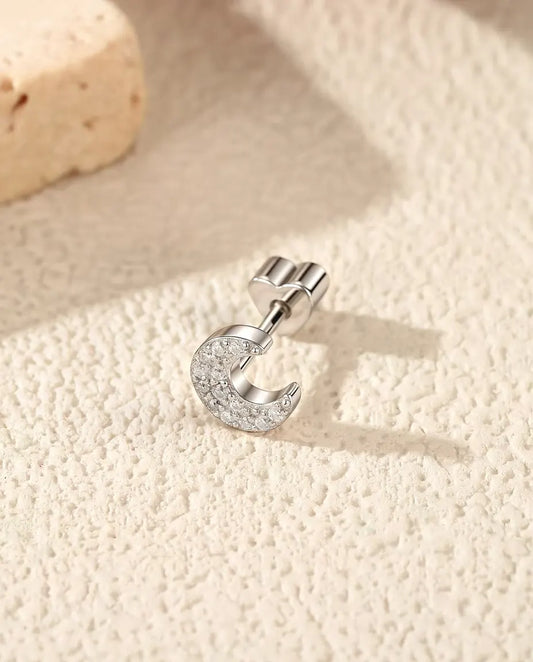 Puces d’Oreilles Croissant de Lune Pavé de Moissanites en Argent 925 - posée sur le côté sur une surface claire texturée, fermoir en forme de cœur sur la tige