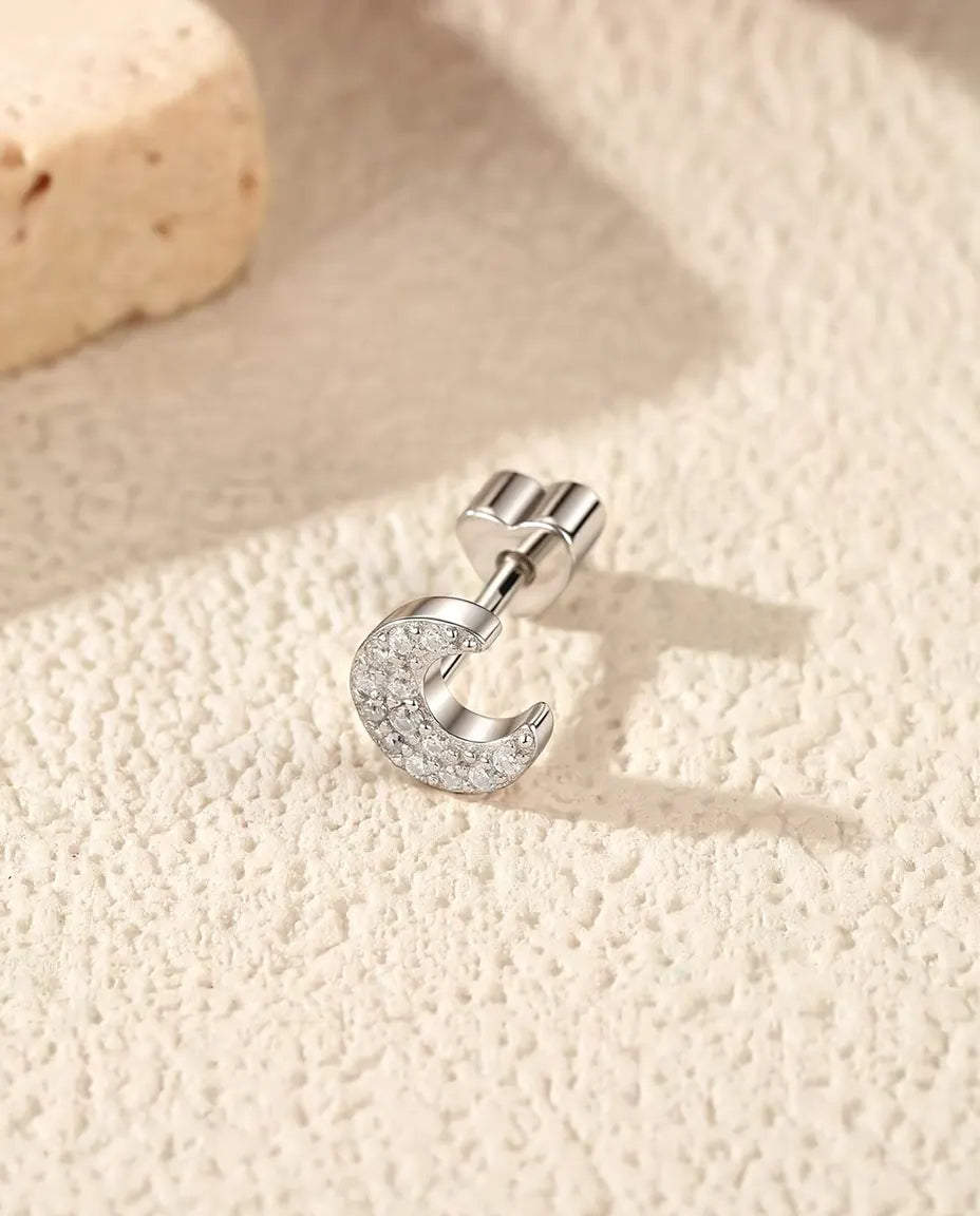 Puces d’Oreilles Croissant de Lune Pavé de Moissanites en Argent 925 - posée sur le côté sur une surface claire texturée, fermoir en forme de cœur sur la tige
