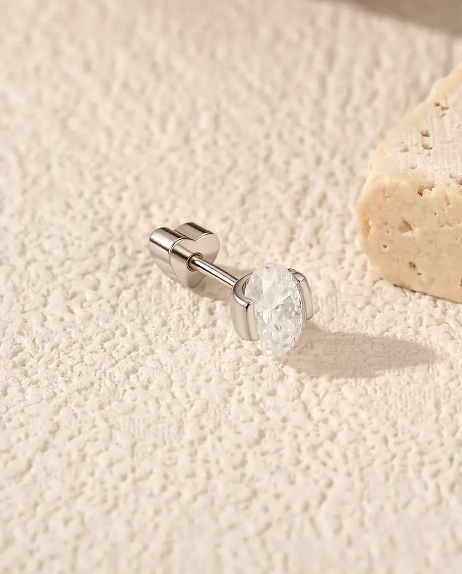 Puces d’Oreilles Moissanite Ovale Serti Latéral en Argent 925 - posée sur le côté sur une surface claire texturée, fermoir en forme de cœur sur la tige