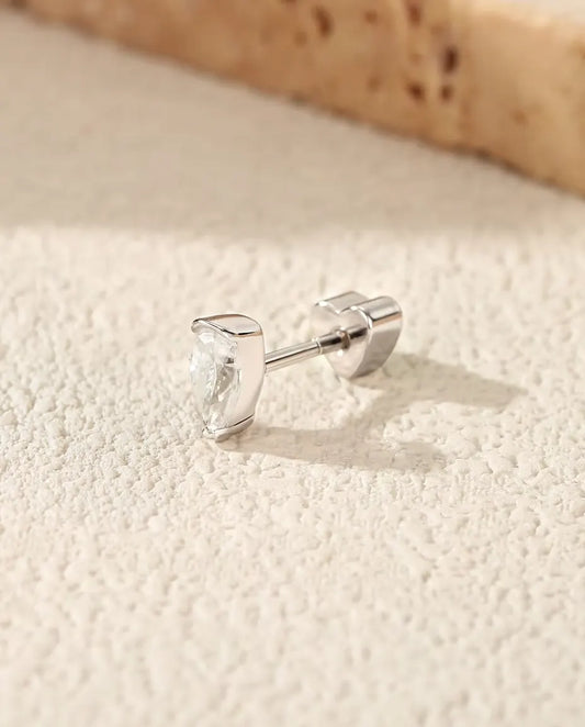 Puces d’Oreilles Moissanite Poire en Argent 925 - posée sur une surface claire texturée près d’une dalle de travertin