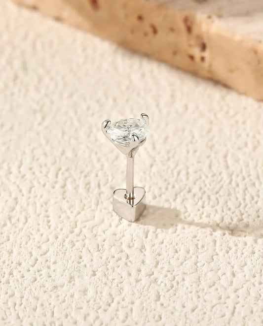 Puces d’Oreilles Moissanite Ronde à Trois Griffes en Argent 925 - debout sur son fermoir en forme de cœur, sur une surface claire texturée