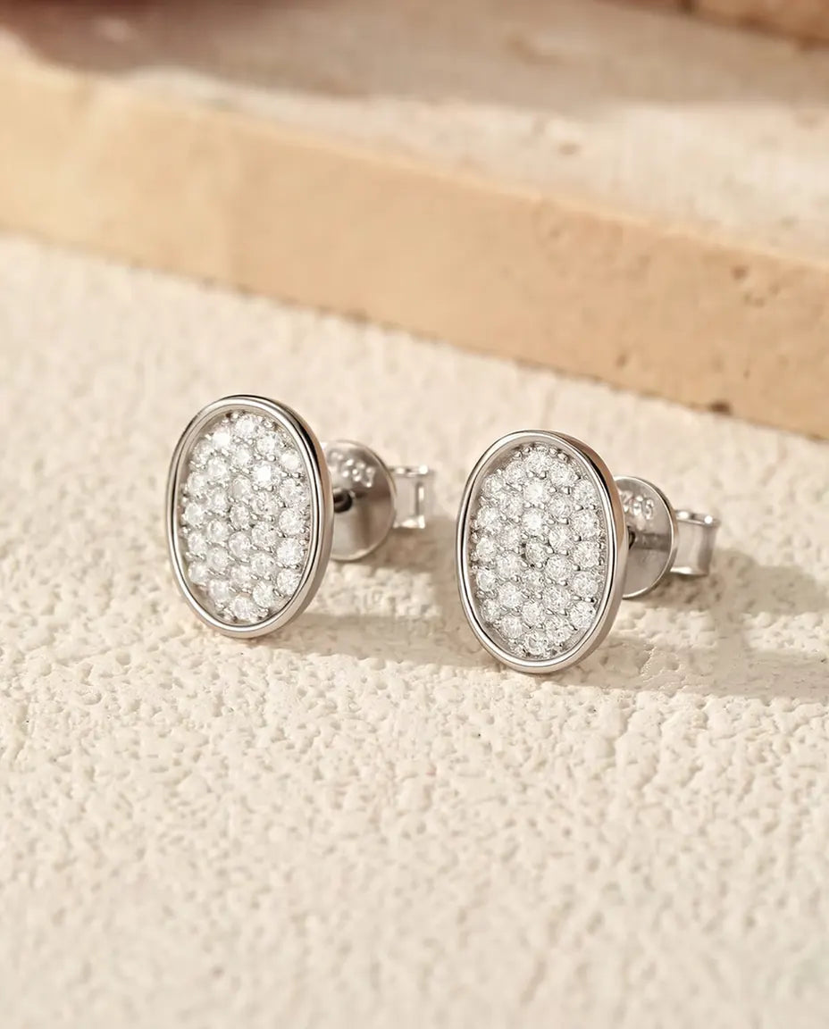 Puces d’Oreilles Ovales Pavées de Moissanites en Argent 925 - la paire posée sur une surface claire texturée