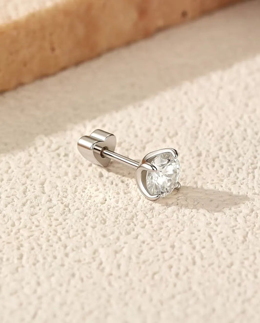 Puces d’Oreilles Solitaire Moissanite 5 mm Quatre Griffes en Argent 925 - posée sur le côté sur une surface claire texturée, fermoir en forme de cœur sur la tige