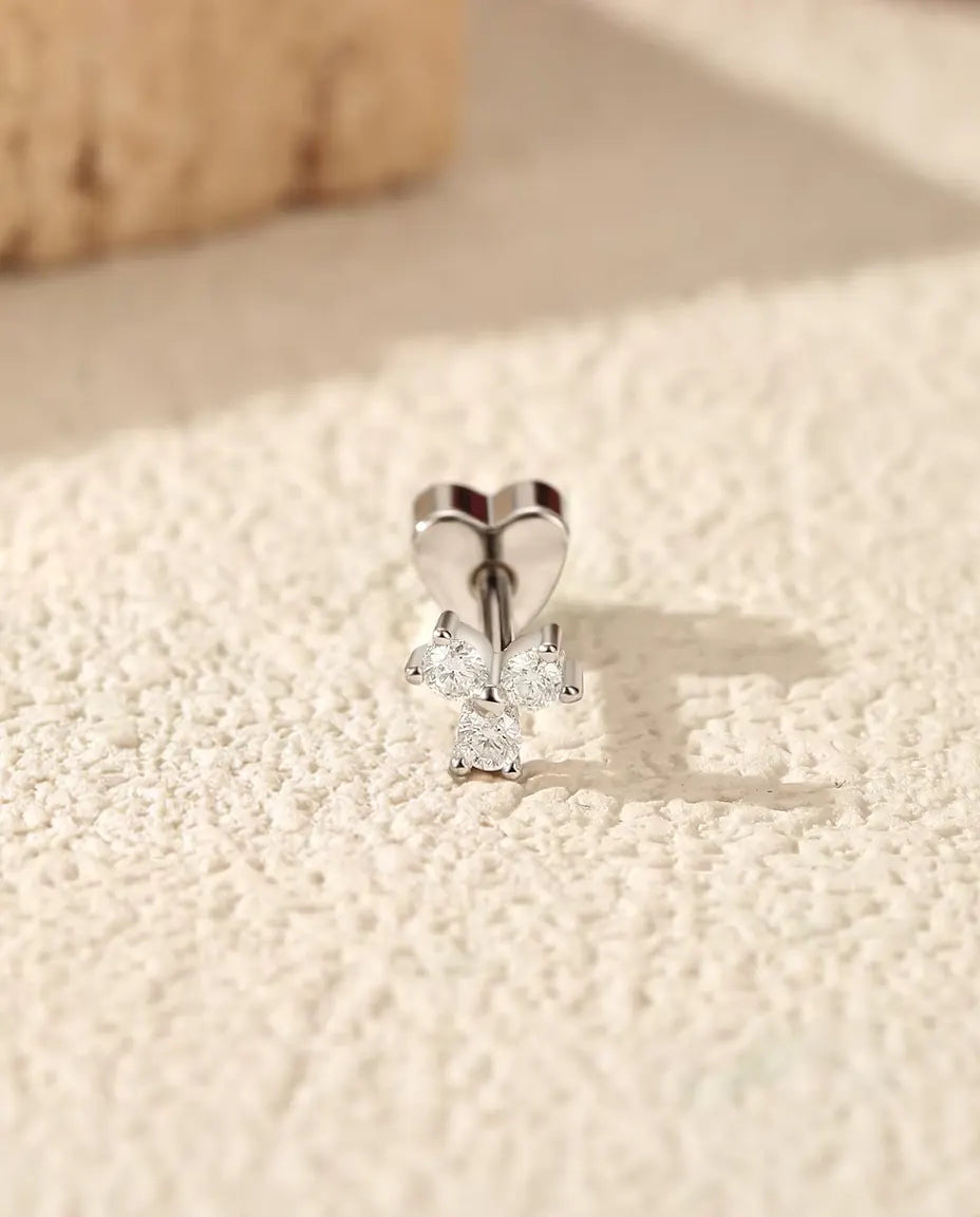 Puces d’Oreilles Trèfle Moissanite en Argent 925 - debout sur son fermoir en forme de cœur, sur une surface claire texturée