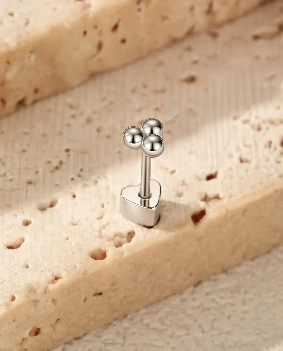 Puces d’Oreilles Trèfle à Trois Billes en Argent 925 - debout sur son fermoir en forme de cœur, sur une surface claire texturée